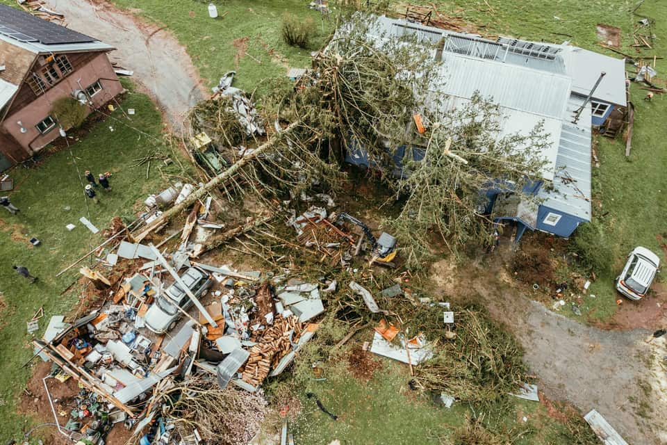 An aerial view of a house wrecked by fallen trees after a storm